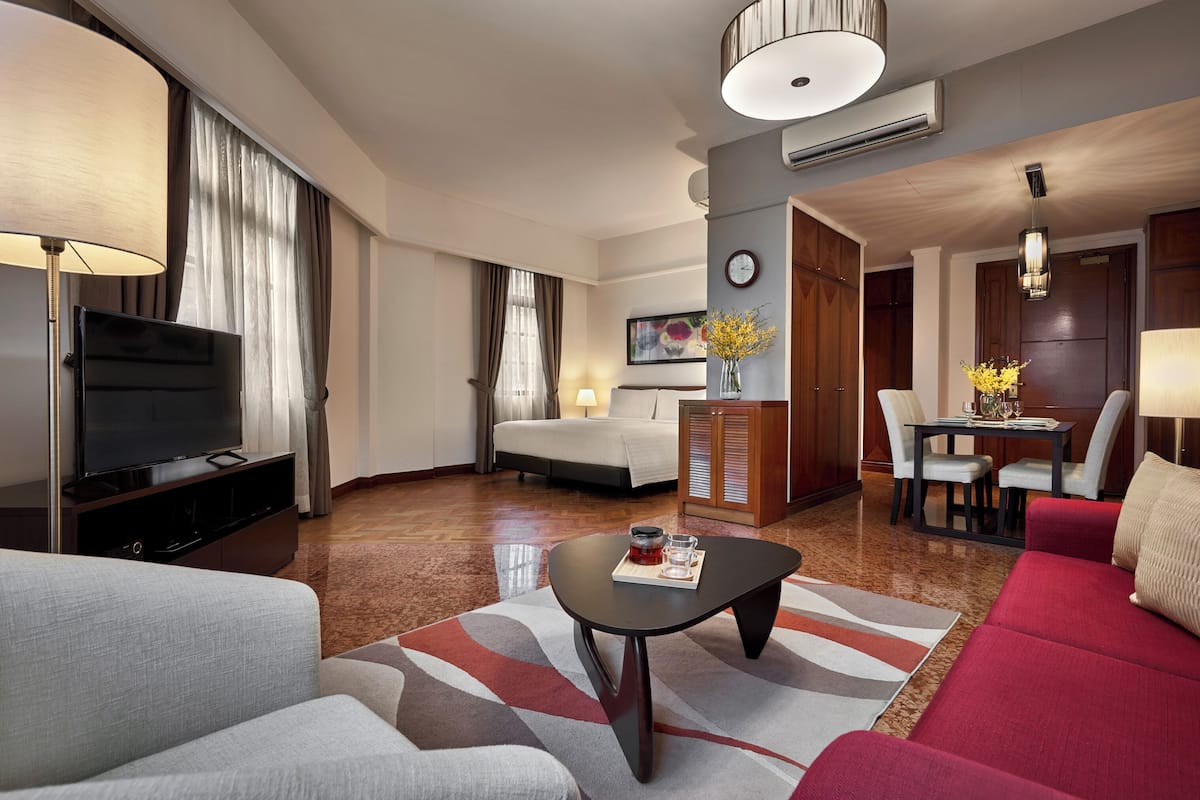 A modern hotel room with a TV, sofa, coffee table, dining area, and a bed.