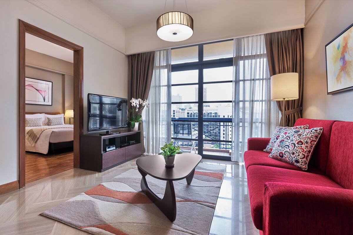 A modern hotel room with a large window, a red sofa, a TV, and a dining table with a plant.