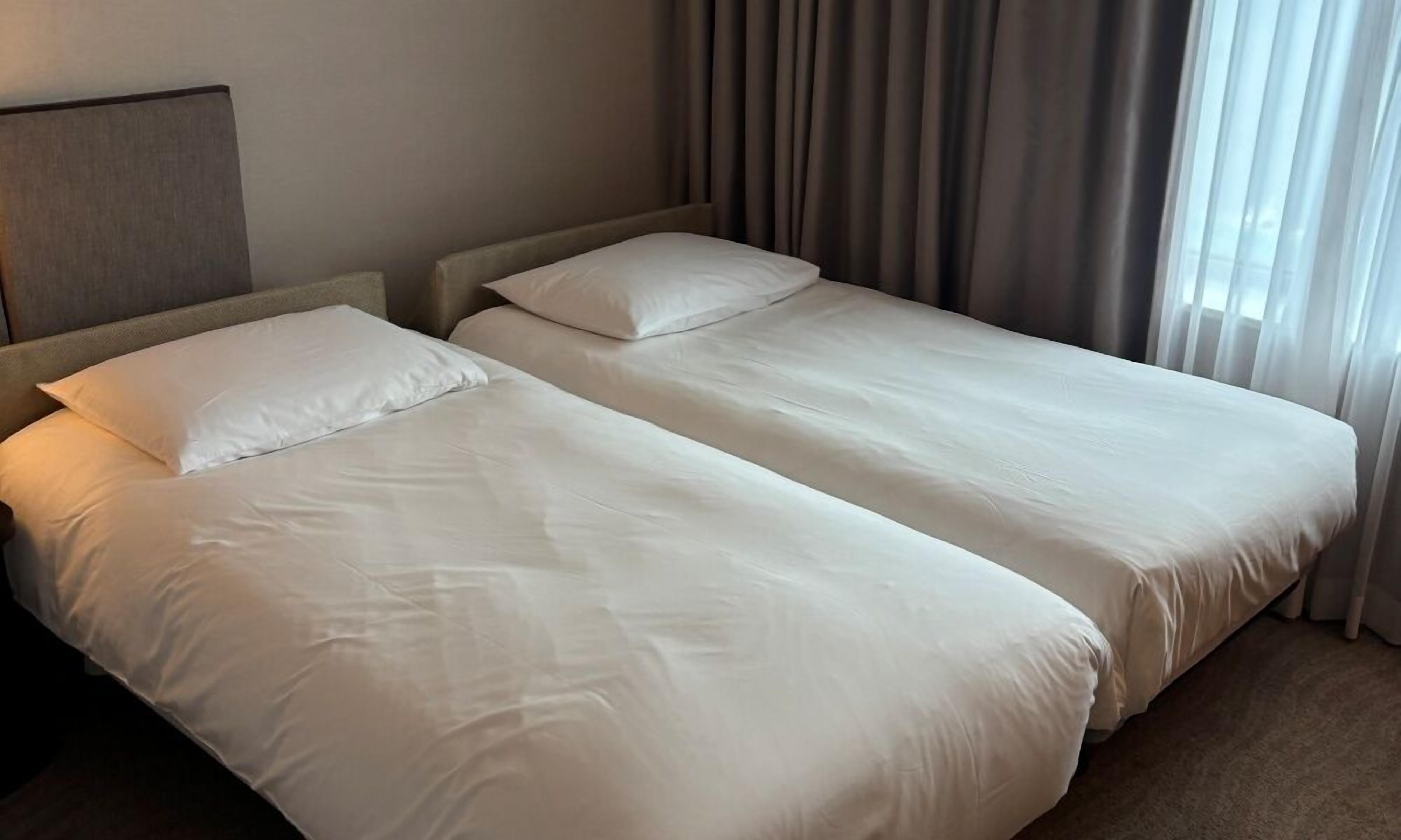 Habitación de hotel con dos camas, cabeceras y una ventana con cortinas.