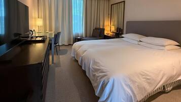 Una habitación de hotel con una cama grande, un escritorio con una silla, un televisor y una lámpara.