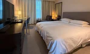 A hotel room with a large bed, a desk with a chair, a TV, and a lamp.