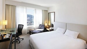 A hotel room with a large bed, a desk, a chair, a small table, and a view of the city. - Samsung Hotel Geoje (Geoje)