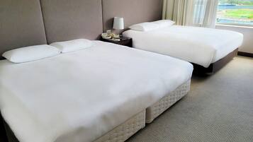 A hotel room with two beds, a nightstand with a lamp, and a view of a lake through the window.