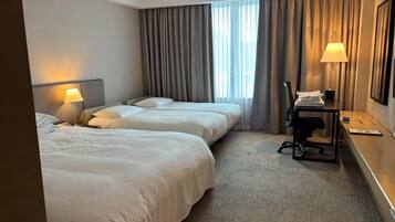 A hotel room with two beds, a desk, a chair, and a window with curtains.