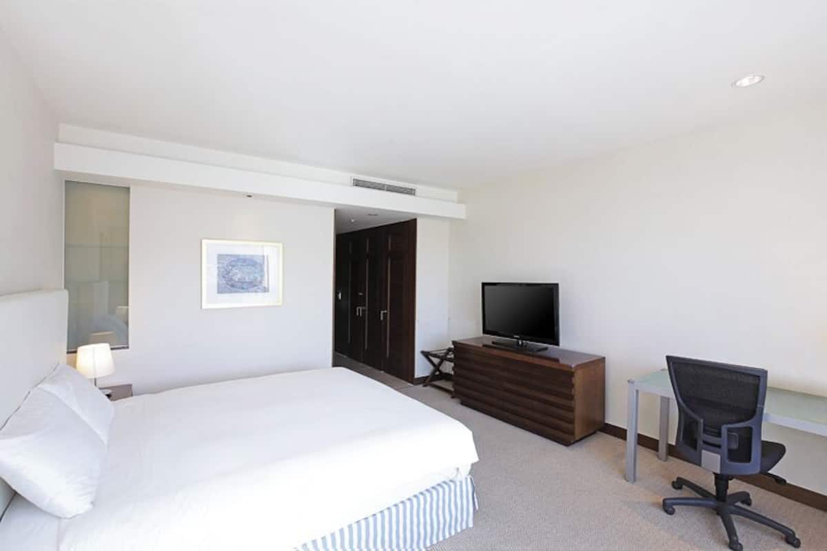 A hotel room with a bed, a TV, a desk, and a chair.