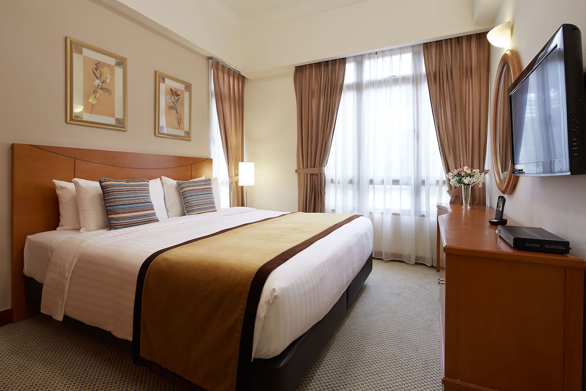 A hotel room with a large bed, a wooden headboard, a flat-screen TV, and a desk with a lamp.