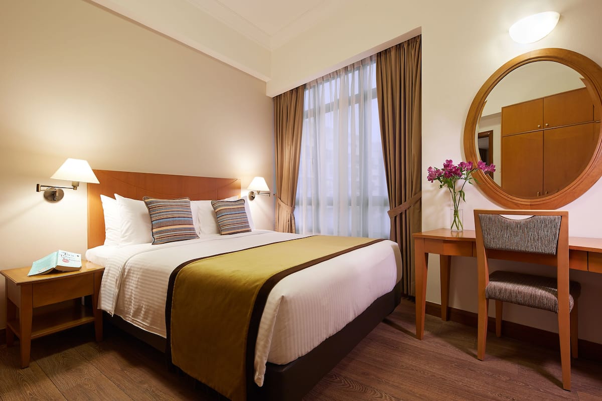 A hotel room with a bed, bedside tables, a desk with a chair, a mirror, and a window with curtains.