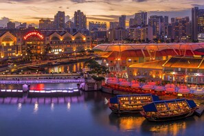 A riverside hotel with a prominent Riverside Point sign, boats docked in the water, and a city skyline in the background.