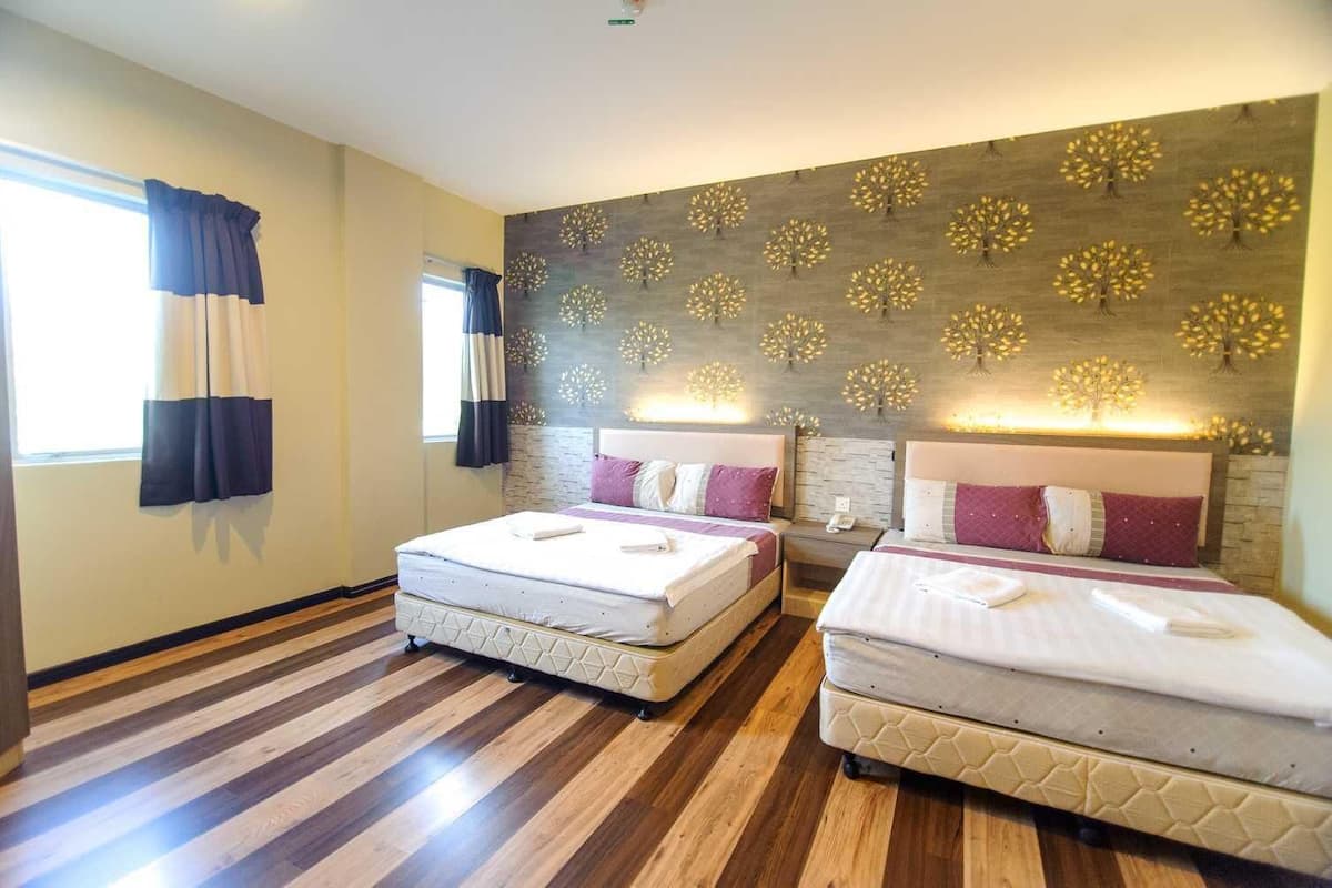 A hotel room with two beds, a wooden floor, a patterned wall, and a window with curtains.