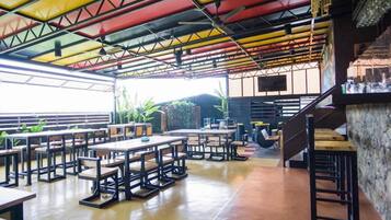 A spacious indoor area with multiple tables and chairs, a staircase, and a large window allowing natural light.