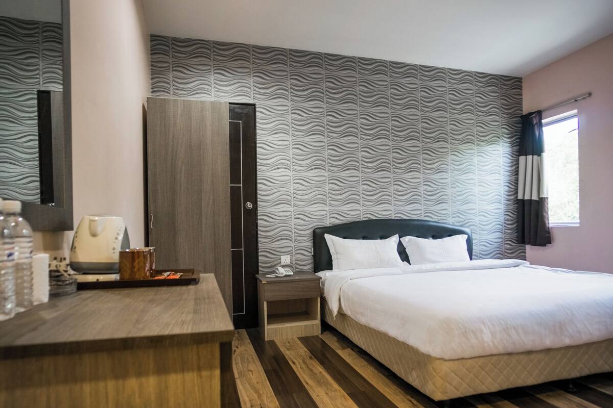A hotel room with a bed, a desk, a wardrobe, and a patterned wall.