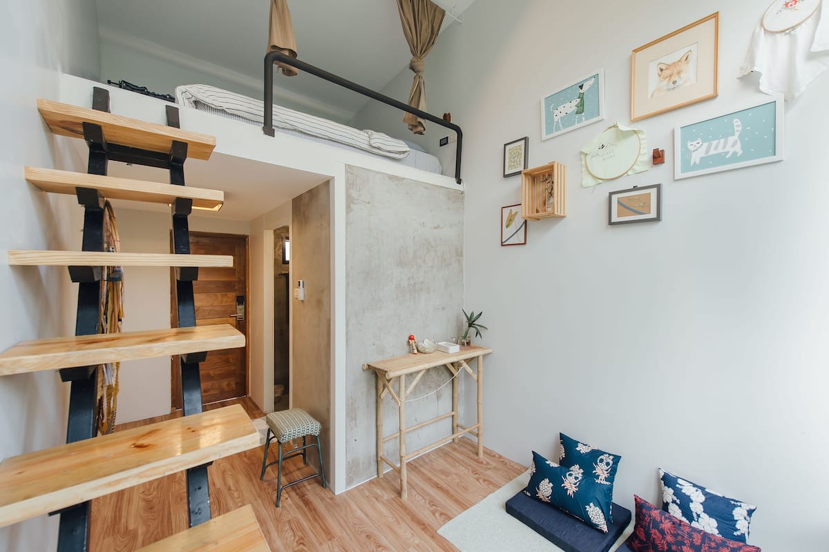 A loft bedroom with a bunk bed, a small desk, and a wall adorned with framed artwork.