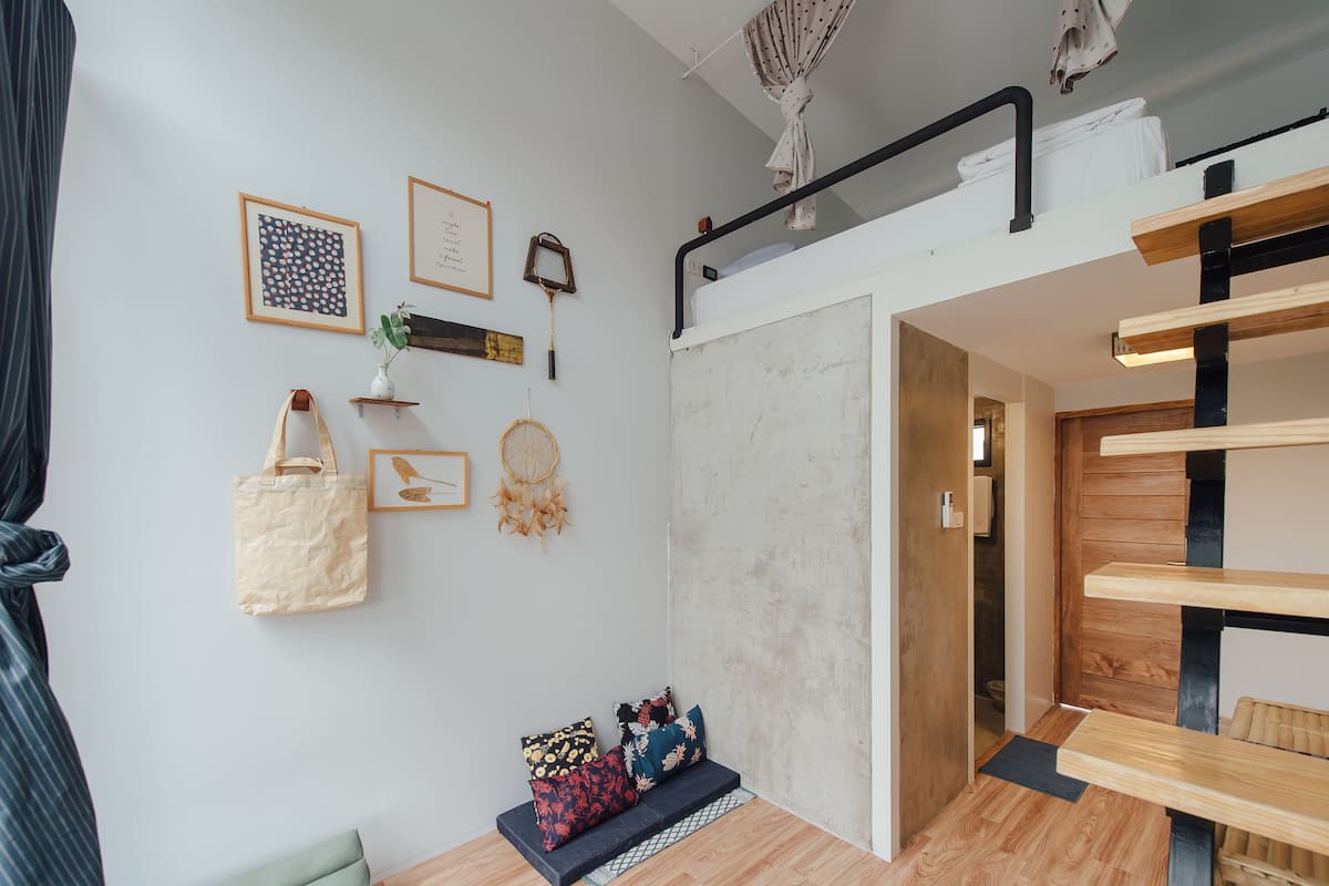 A room with a bunk bed, a small seating area with cushions, a wall with framed pictures, and a hanging dreamcatcher.