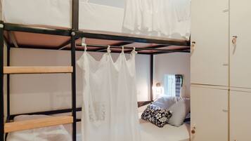 Una cama litera con dosel, una cama individual con almohada floral y un armario con cerradura.