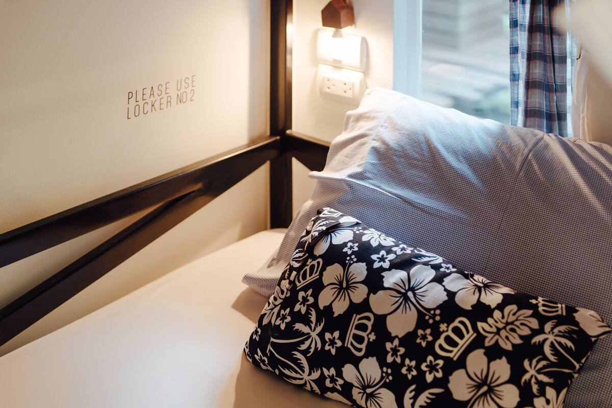 A hotel room with a bed, a pillow with a floral pattern, a wall-mounted light switch, and a sign instructing to use locker number 02.