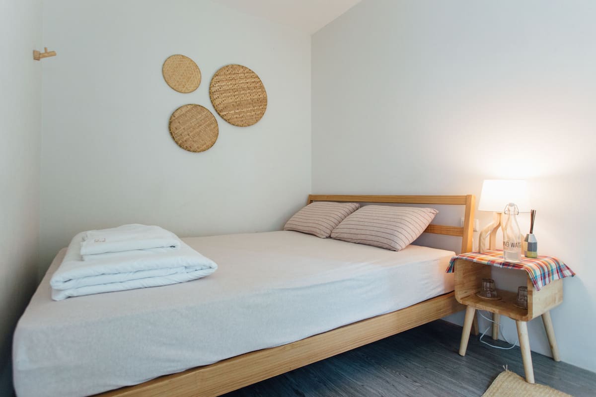 A neatly made bed with a white duvet, a wooden headboard, and a bedside table with a lamp and a bottle.