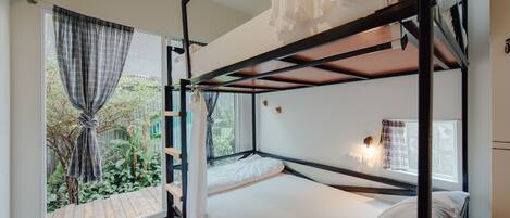 Dormitorio con literas, una ventana, una cortina y una mesita con lámpara.