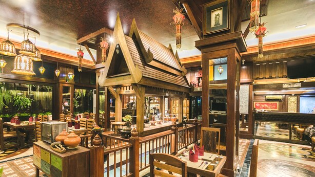 Un décor intérieur traditionnel en bois, avec des tables et des chaises, un coin bar et des lanternes suspendues.