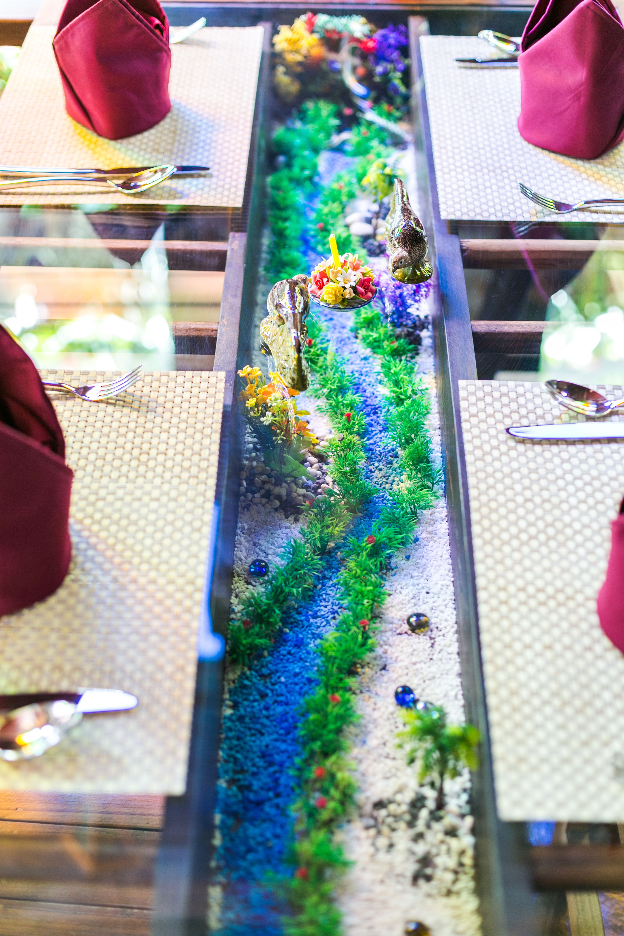 Una mesa de comedor con un centro decorativo que presenta un paisaje en miniatura con rocas, plantas y un pequeño pájaro.