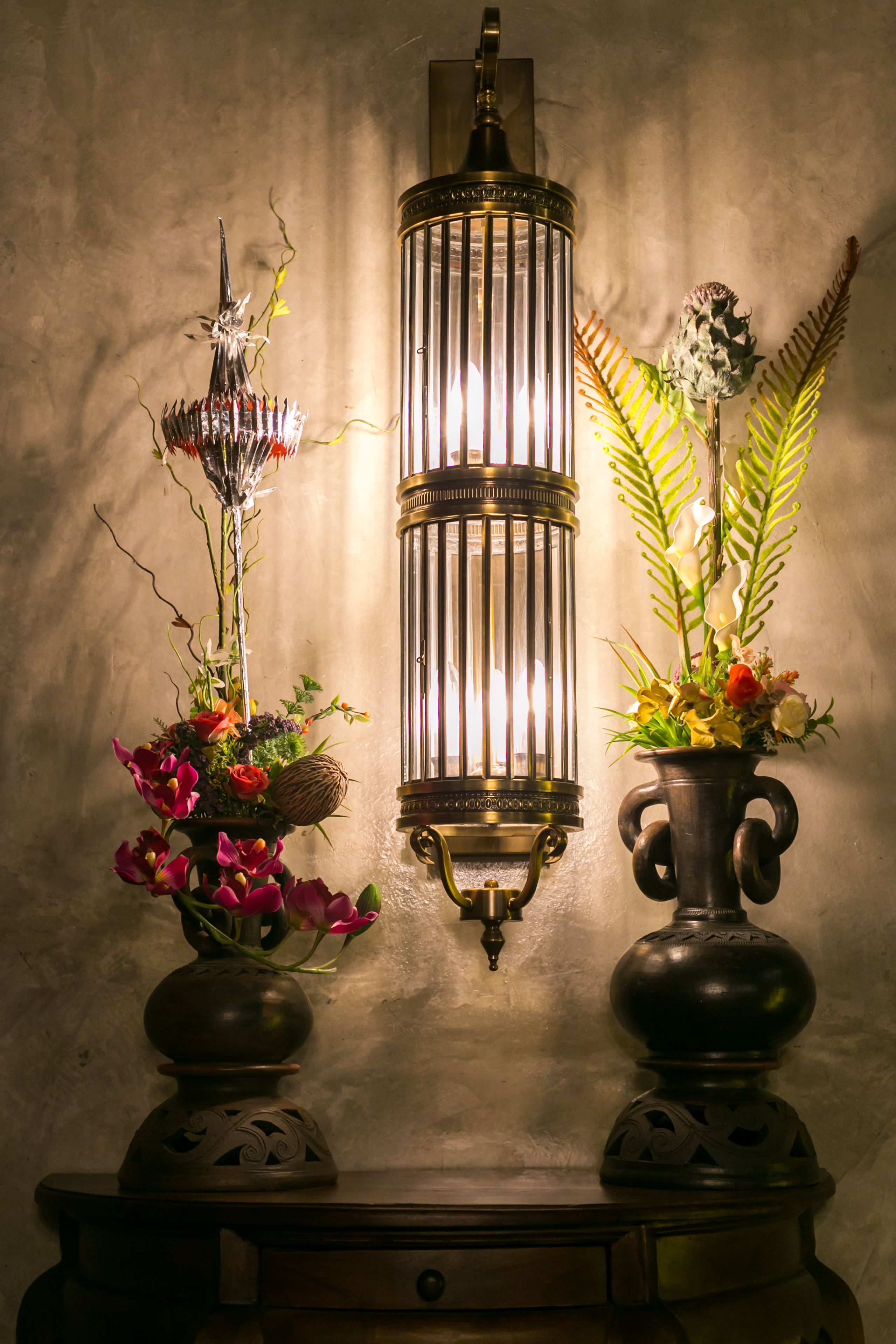 A wall-mounted lantern with a candle holder and two vases with flowers.