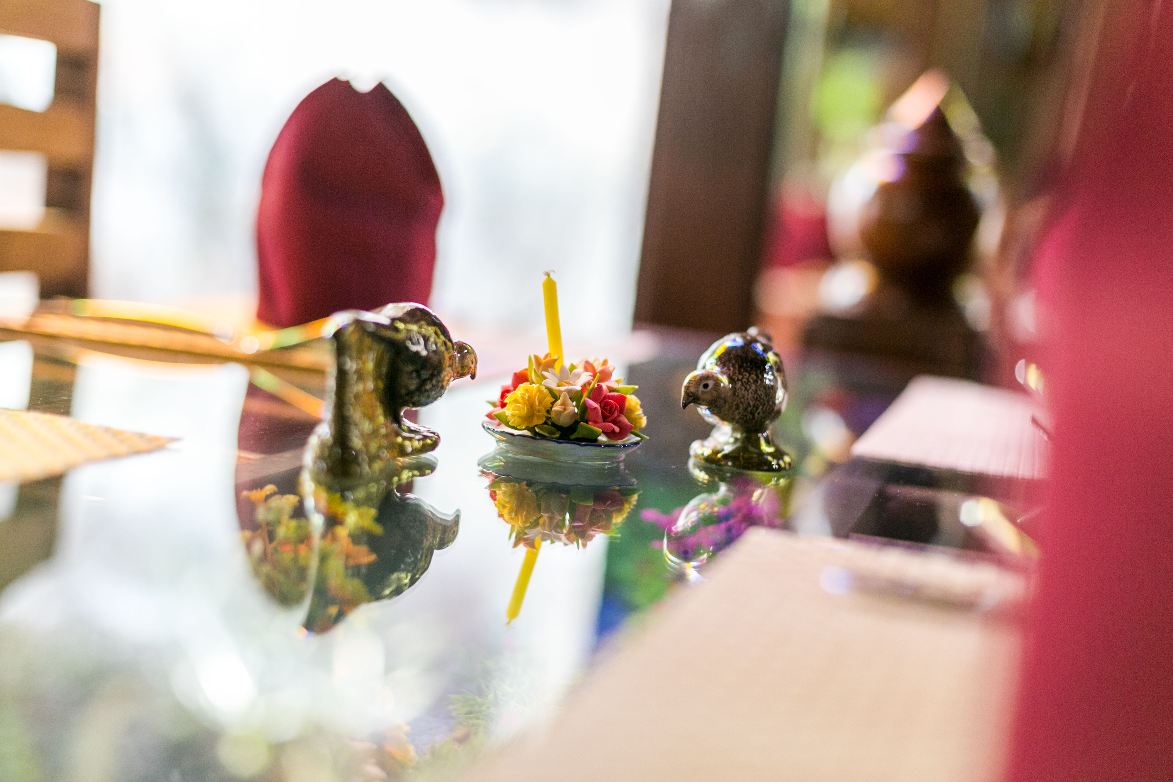 Mesa de vidro reflectora com objetos decorativos, incluindo uma pequena tigela de flores e duas figuras de animais.