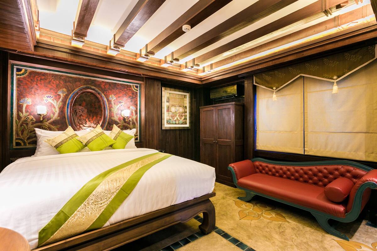 Ein großes Bett mit einer grün-weißen Tagesdecke, ein rotes, gepolstertes Sofa und ein großes Wandbild.