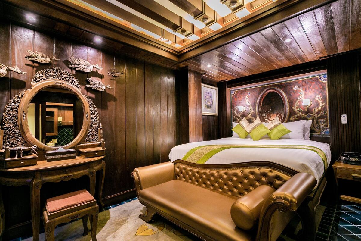 Ein Zimmer mit einem großen Bett, einem hölzernen Schminktisch, einem Spiegel und einer Wandverzierung.
