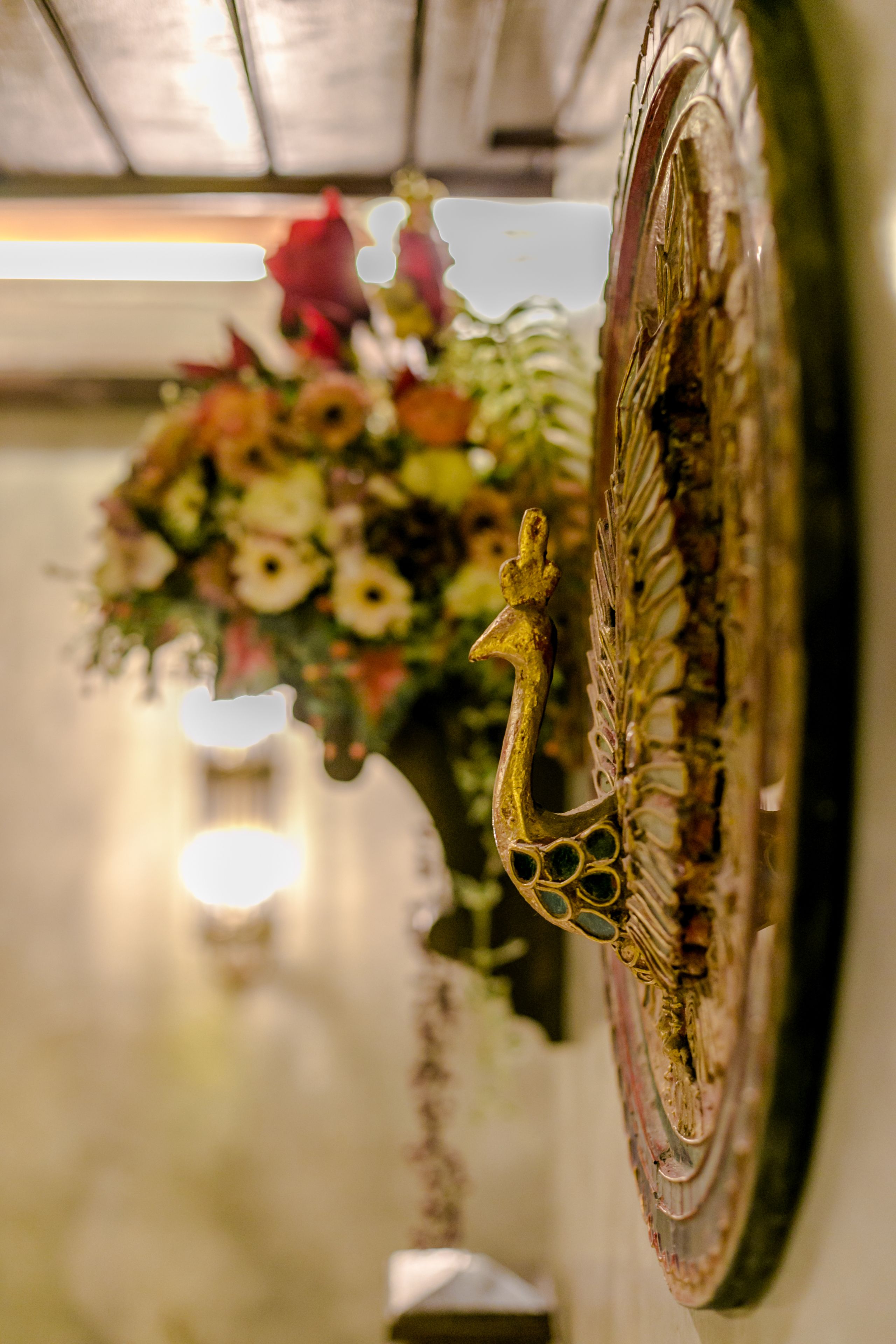 A close-up of a bicycle wheel with a decorative handlebar and a floral arrangement in the background.