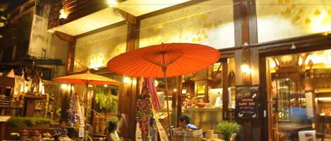 An outdoor market with tables and umbrellas, a sign for a restaurant, and various stalls.