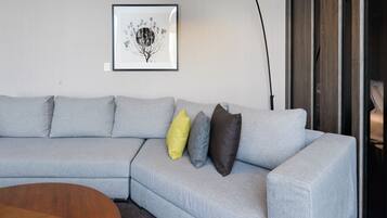 Ein modernes Wohnzimmer mit einem grauen Ecksofa, einem Holztisch, einer schwarzen Stehlampe und einem gerahmten Kunstwerk an der Wand.