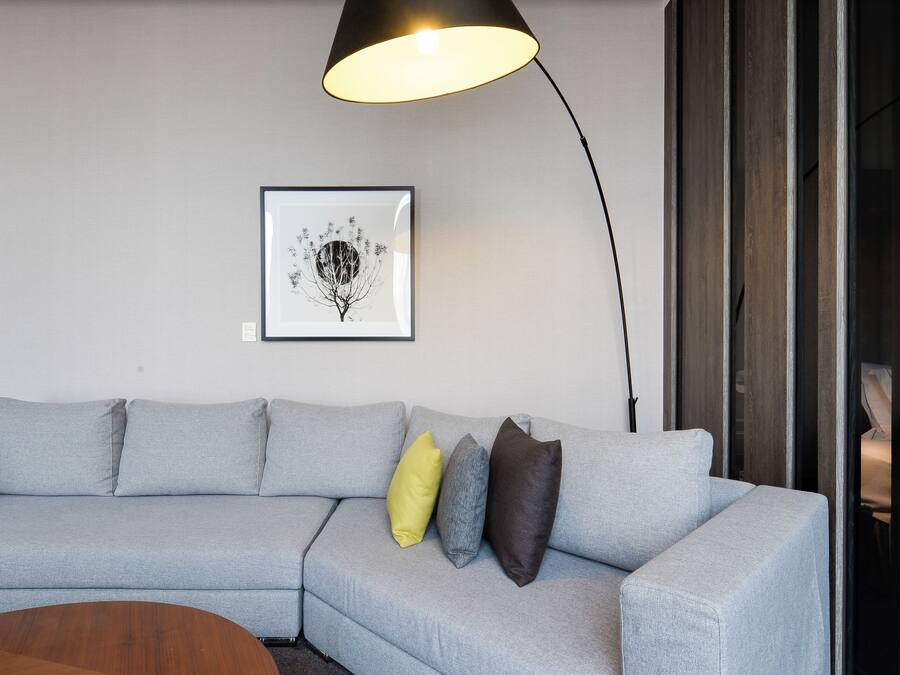 Ein modernes Wohnzimmer mit einem grauen Ecksofa, einem Holztisch, einer schwarzen Stehlampe und einem gerahmten Kunstwerk an der Wand.