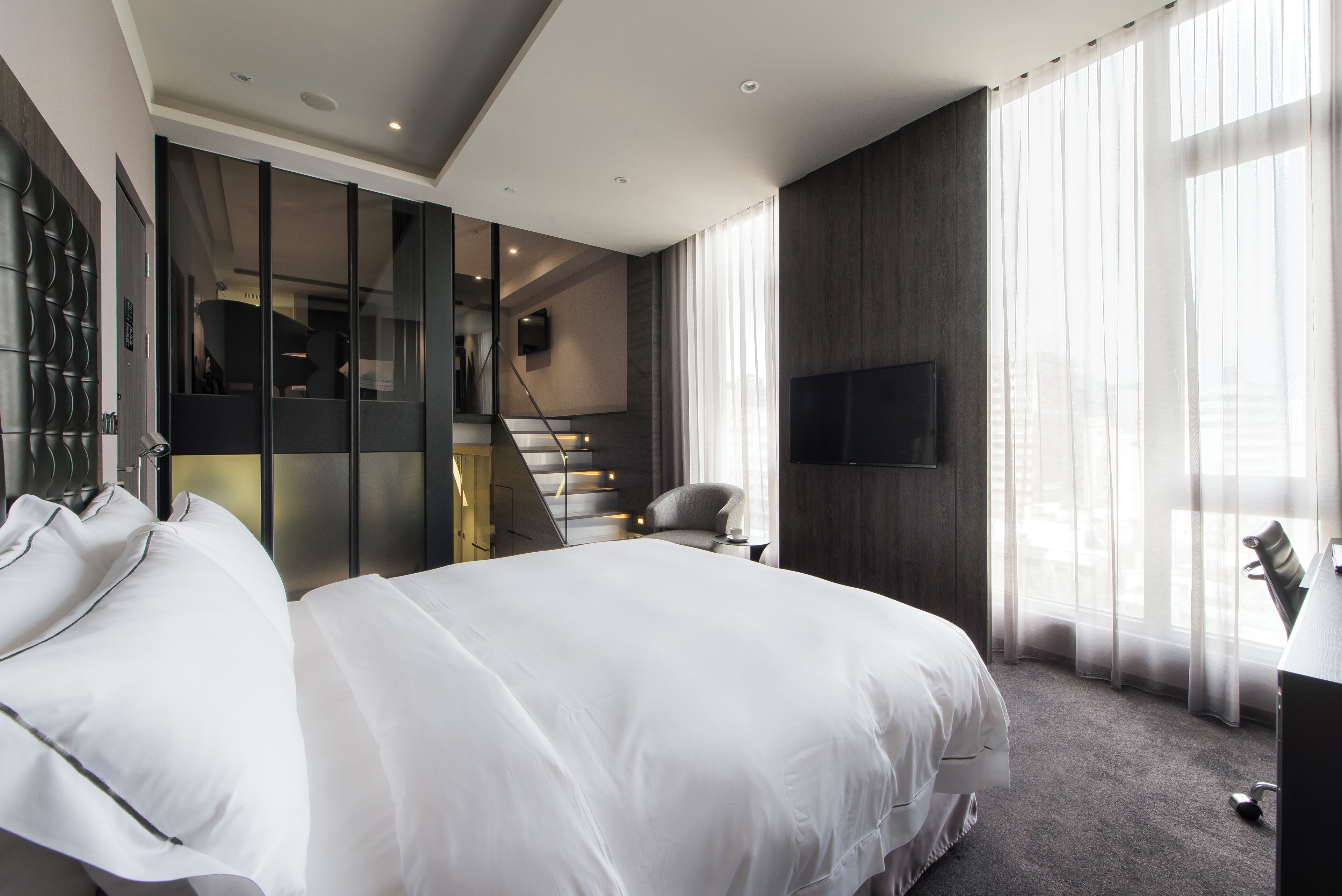 Een moderne hotelkamer met een groot bed, een televisie en een trap naar een hoger niveau.