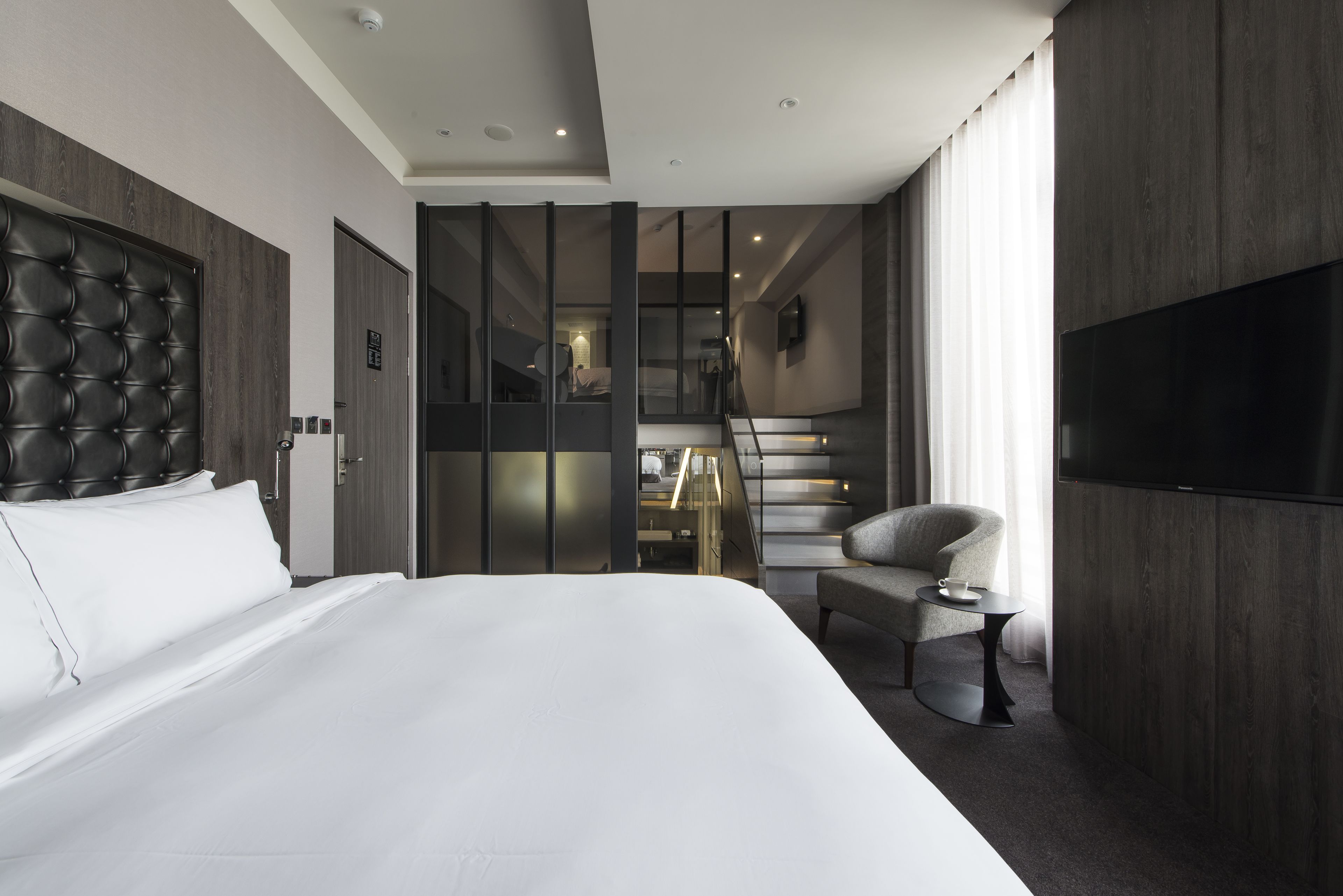 Camera d'albergo moderna con un letto grande, una televisione e una scala che conduce a un piano superiore.