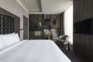 Camera d'albergo moderna con un letto grande, una televisione e una scala che conduce a un piano superiore.