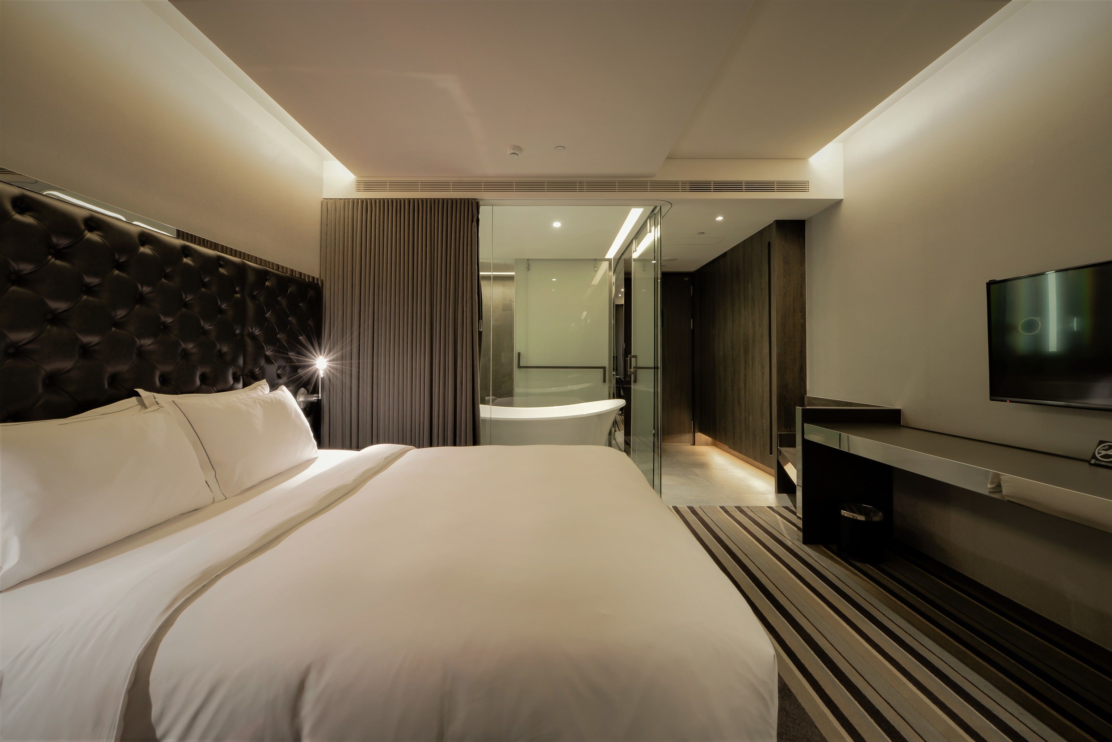 A modern hotel room with a large bed, a flat-screen TV, a bathroom with a bathtub, and a walk-in closet.