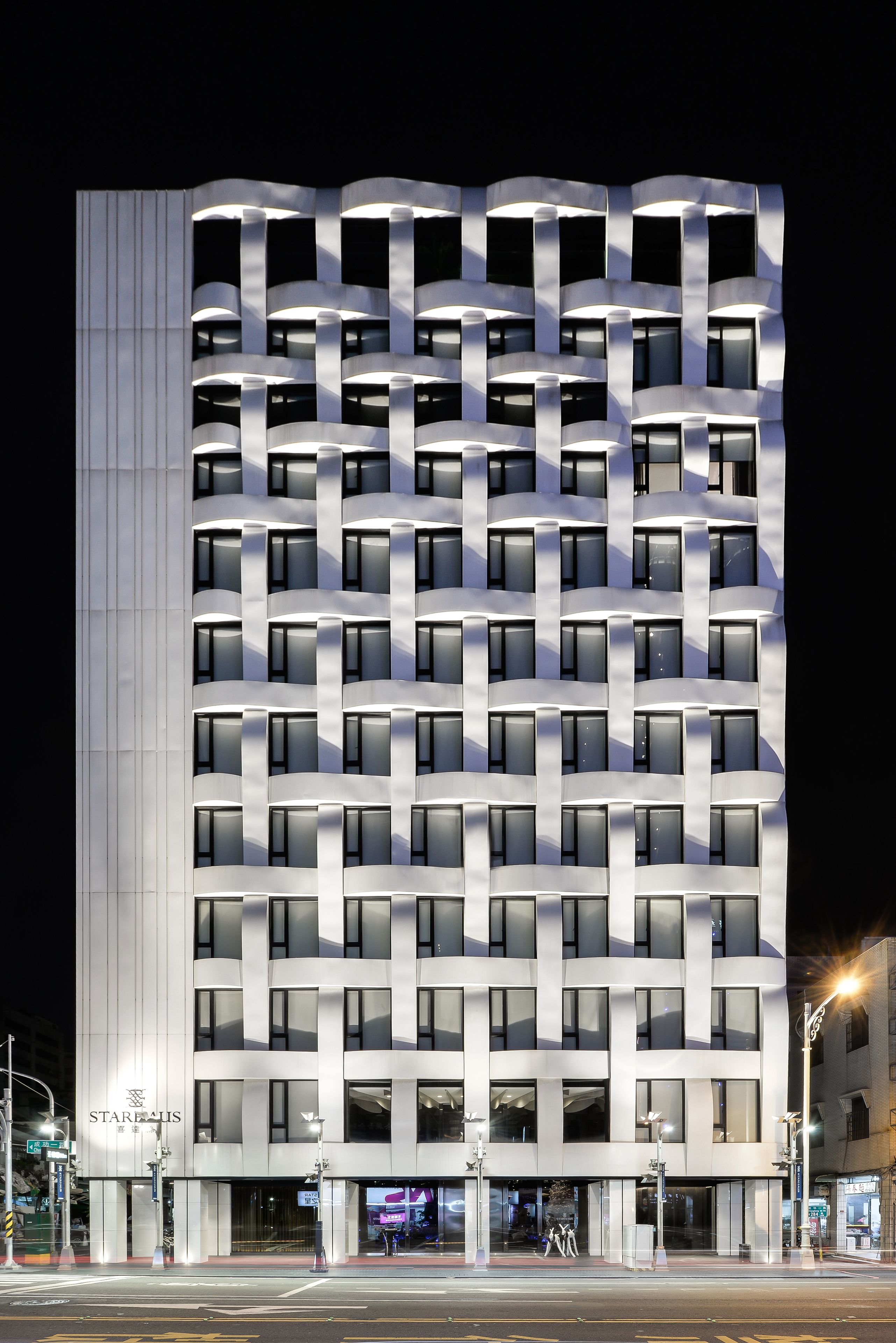 A modern hotel with a grid-like facade, multiple balconies, and a prominent entrance with a sign.