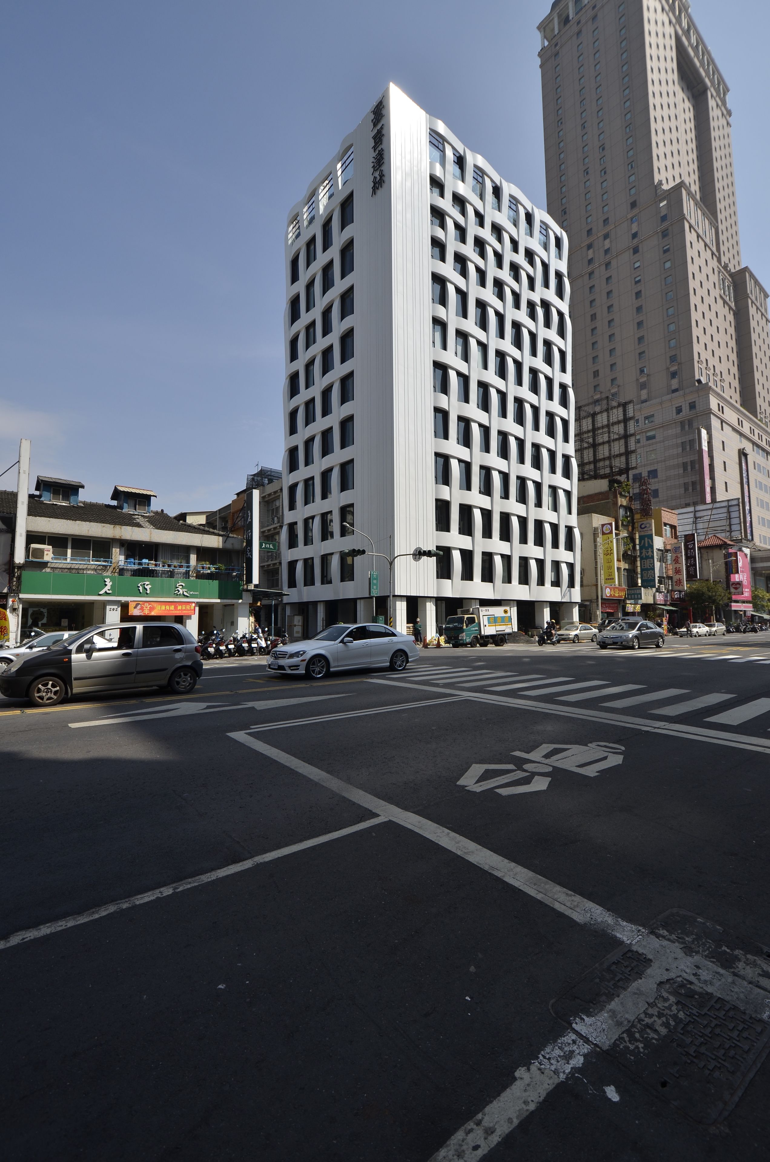 A multi-story building with a grid-like facade, a crosswalk, and vehicles on the street.