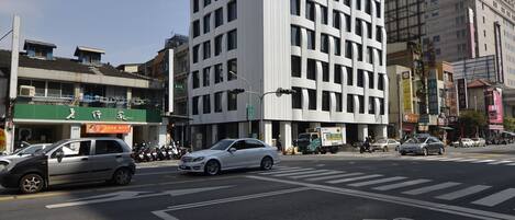 A multi-story building with a grid-like facade, a crosswalk, and vehicles on the street.