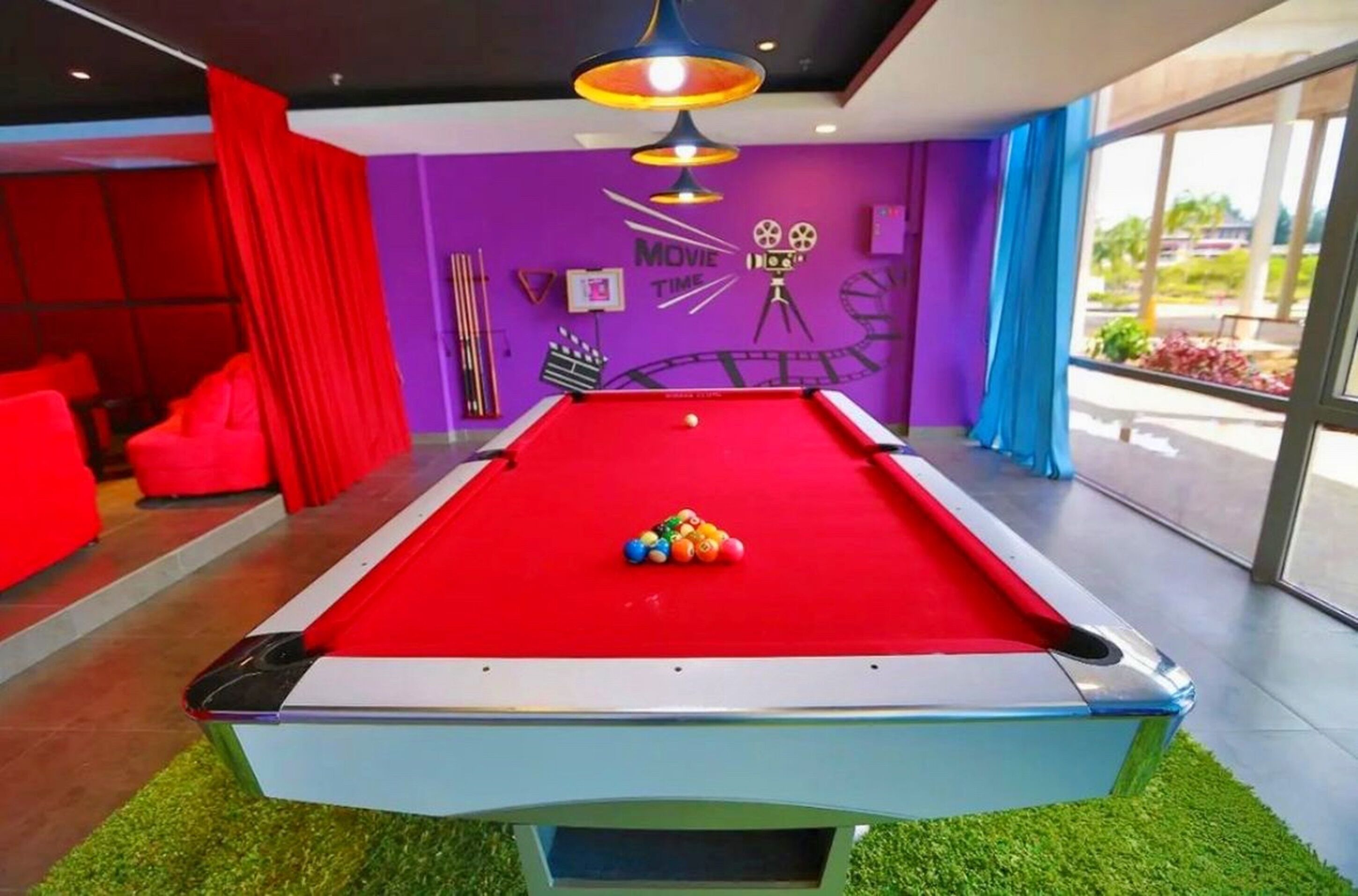 Een biljarttafel met een rode viltkleed, omringd door een paarse muur met decoraties met filmthema.