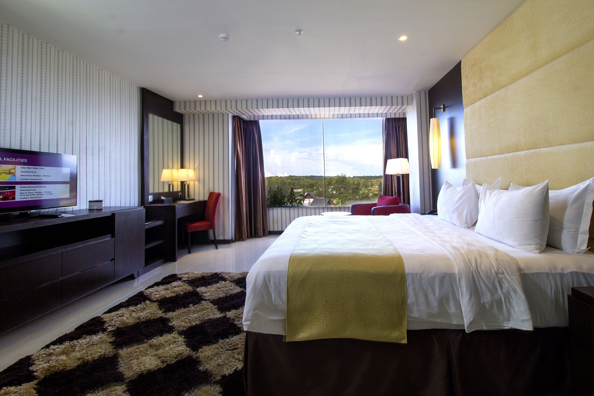 A hotel room with a large bed, a desk, a TV, and a view of the outdoors.