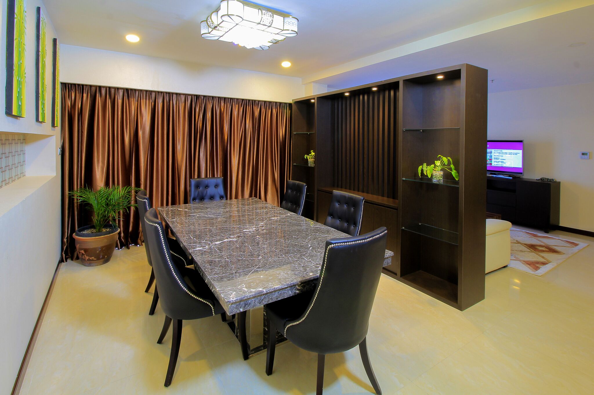 A dining area with a marble table, black chairs, a potted plant, and a television on a stand.