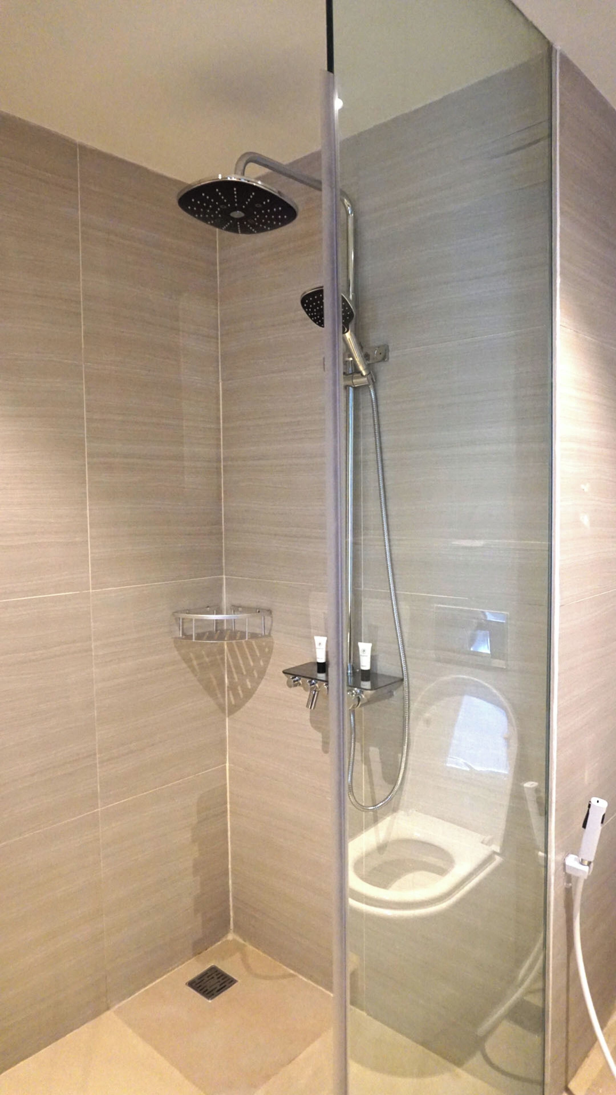 A glass-enclosed shower with a handheld showerhead and a wall-mounted rain showerhead.
