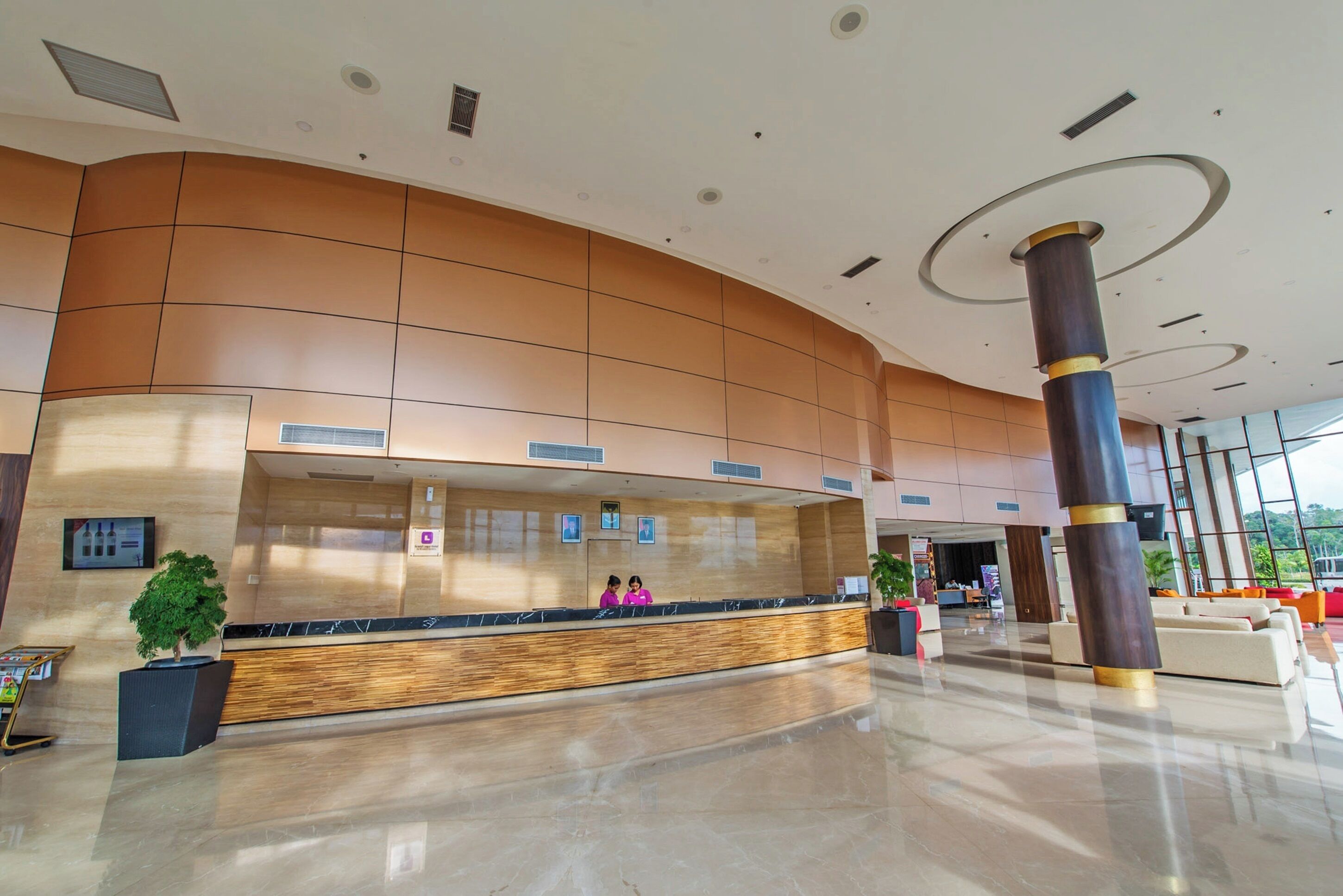 A modern hotel lobby with a reception desk, a large column, and a seating area.