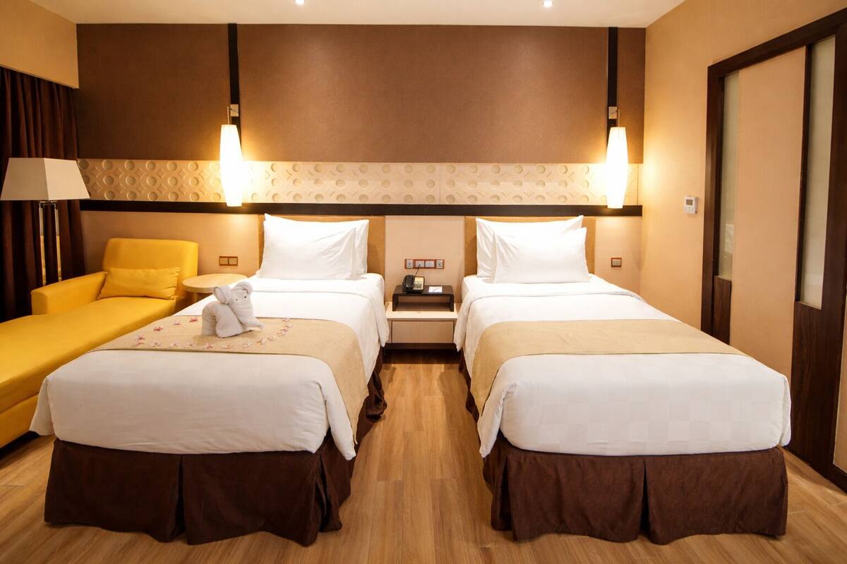 A hotel room with two beds, a sofa, a nightstand, and a lamp.