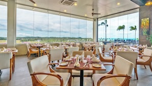 A spacious dining area with multiple tables and chairs, large windows offering a view of the landscape, and ceiling fans.