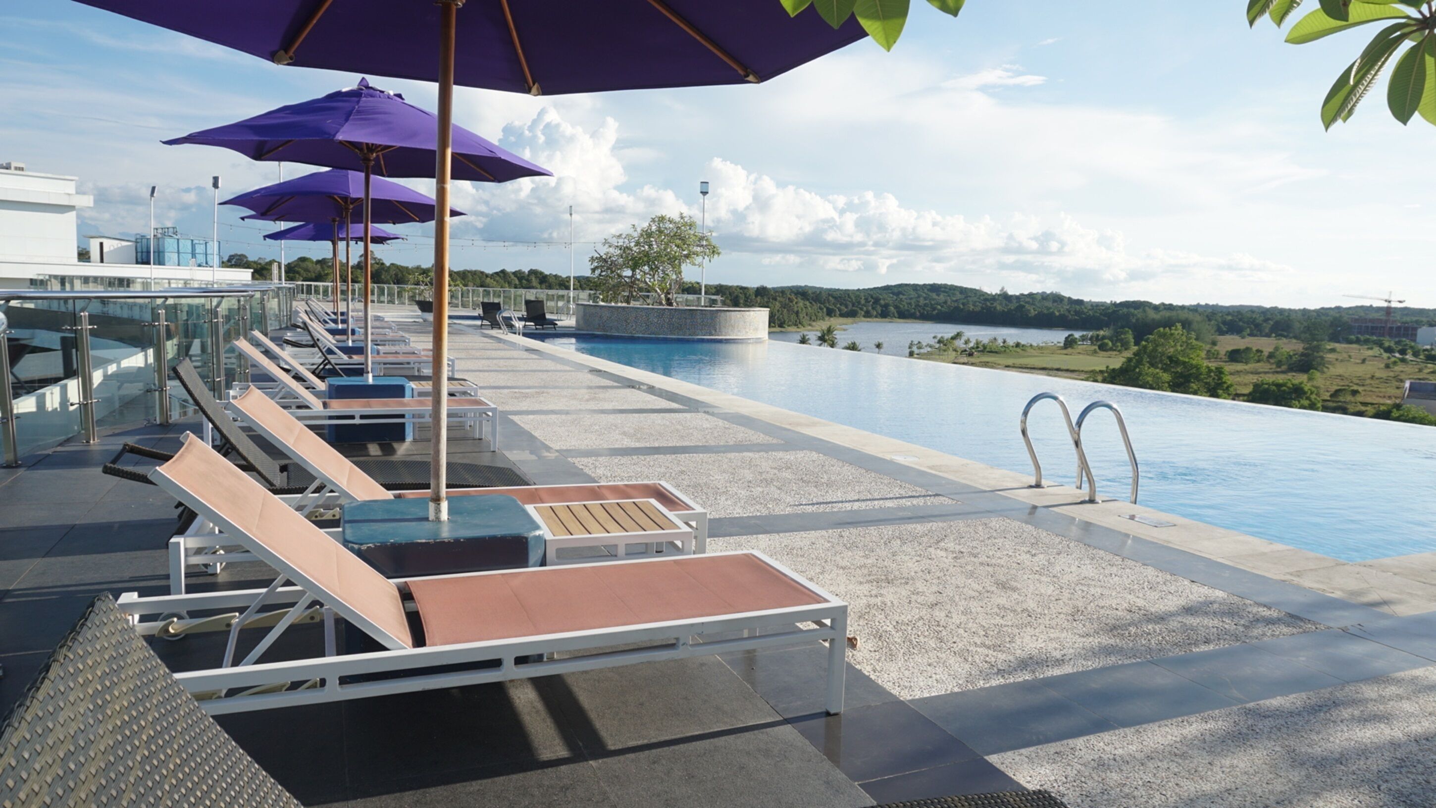 Un área de piscina en la azotea con sillones de descanso y sombrillas, una vista despejada del paisaje circundante y un diseño arquitectónico moderno.
