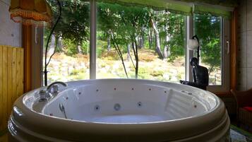 A large, freestanding hot tub with a view of a wooded area through a large window.