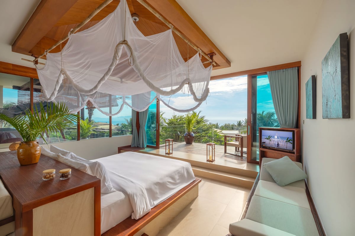 Ein Schlafzimmer mit Bett, Fernseher, Balkon und Blick sowie einer Pflanze.