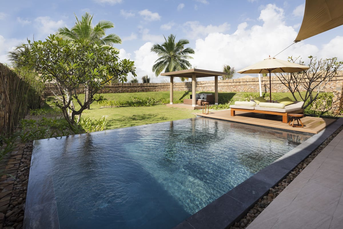 Ein moderner Infinity-Pool mit Steinrand, Holzterrasse und überdachter Sitzgruppe mit Baldachin.
