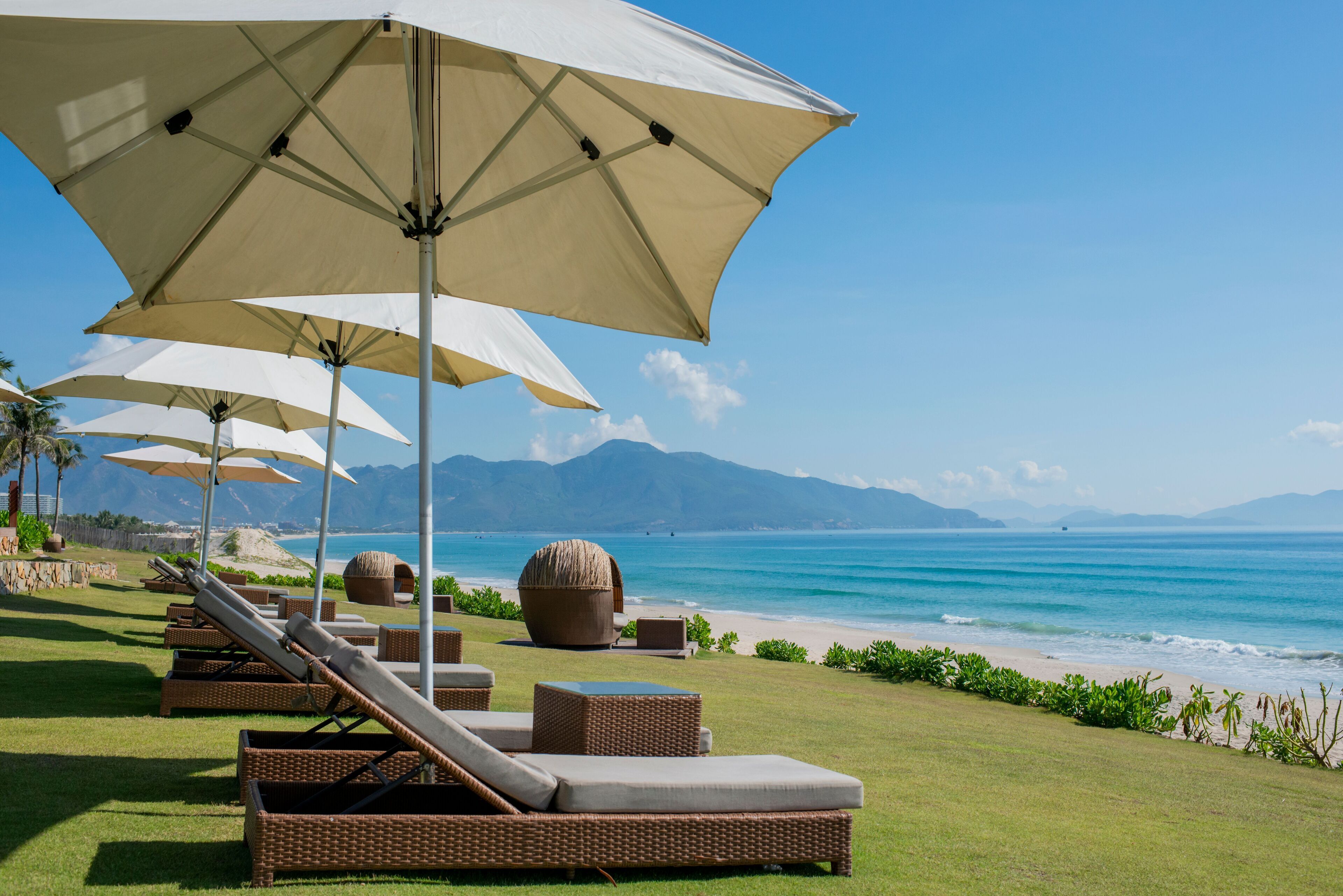 Un espace de détente aménagé sur la plage, avec des chaises longues et de grands parasols, offrant une vue sur l’océan.